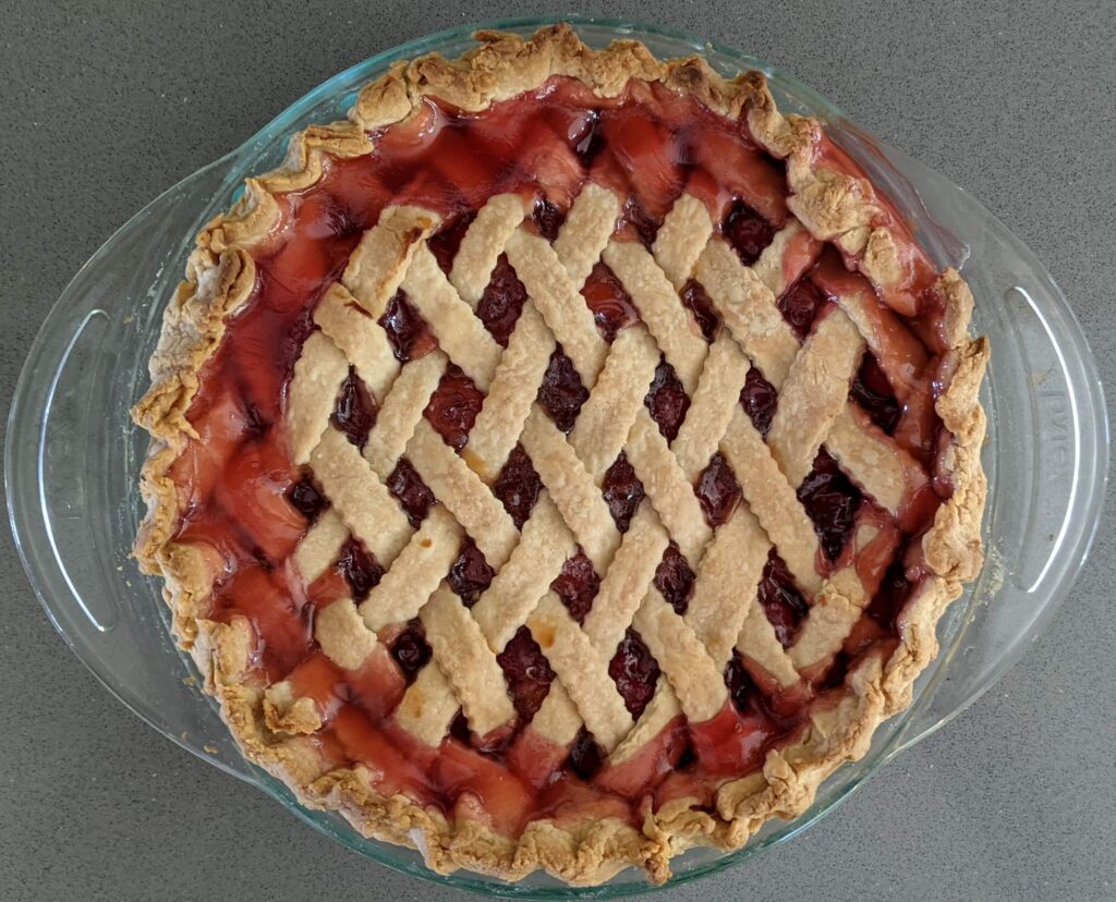 A cherry pie with red filling oozing through a tight diagonal lattice crust
