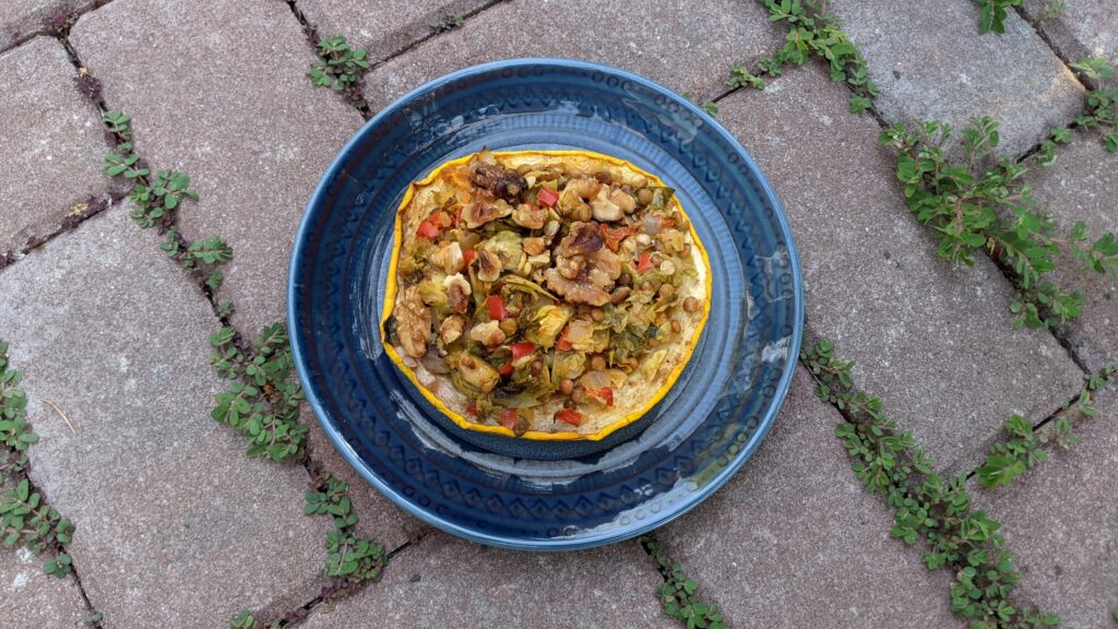 Colorful stuffing fills a bright yellow disk of pattypan squash on a blue plate in a brick-paved garden.