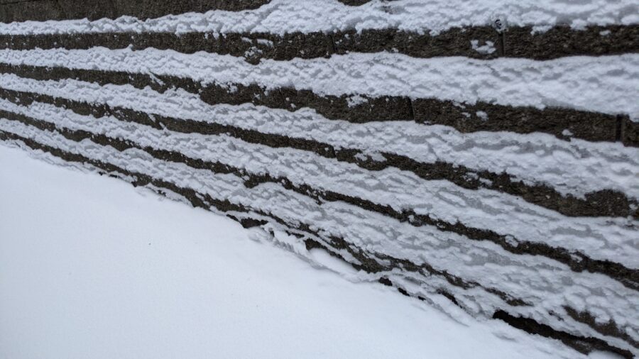 A winter 2021 photograph of a retaining wall covered in terraced rows of snow and ice loosely resembles a music staff.